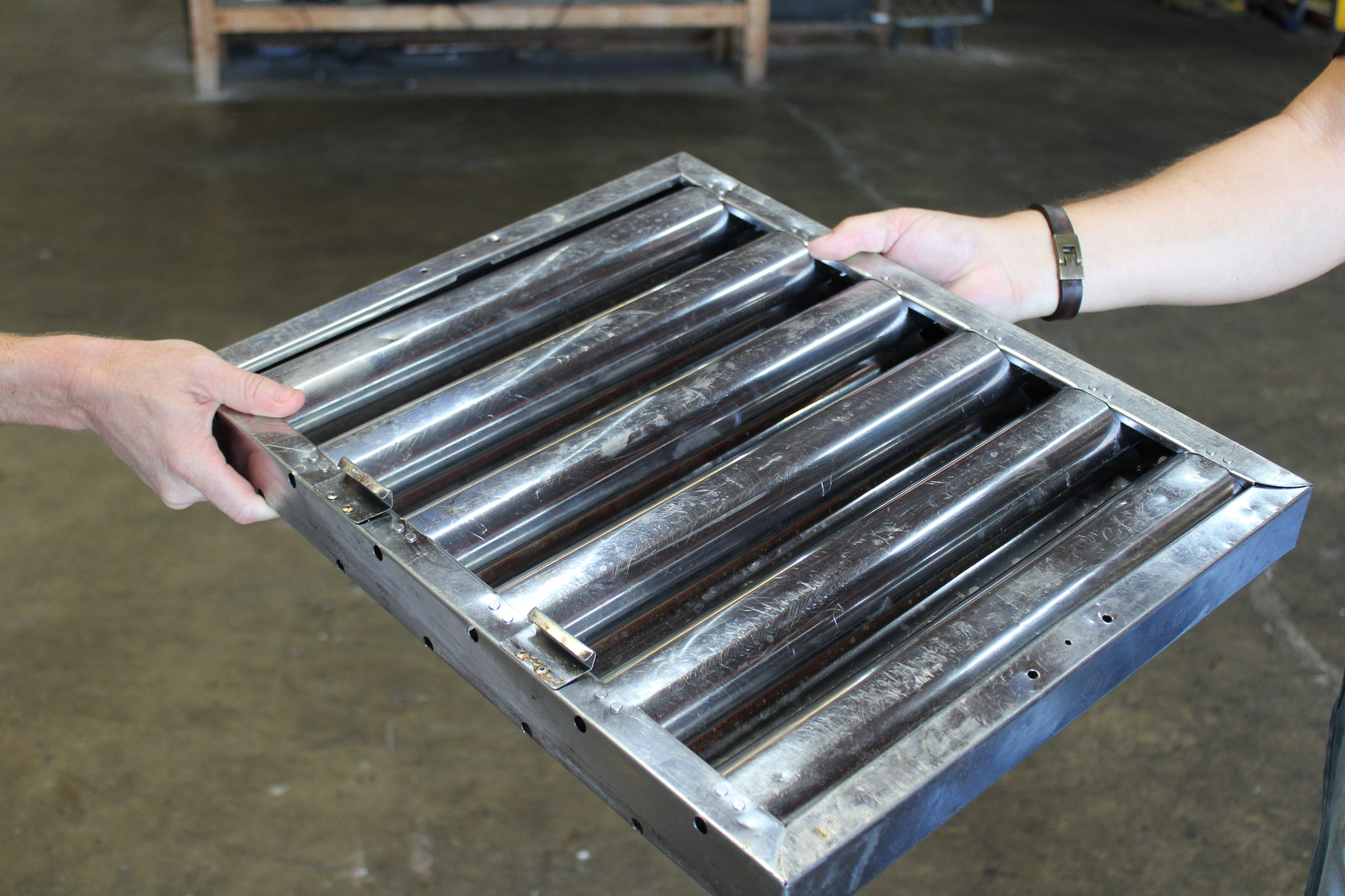Technician holding a cleaned stainless steel baffle hood filter in the Kitchen Guard shop