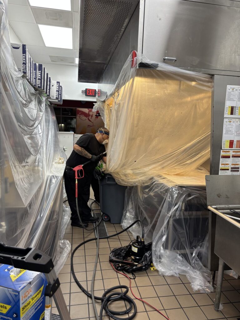 Kitchen Guard of El Paso technician pressure washing a restaurant hood with plastic sheeting protecting the kitchen