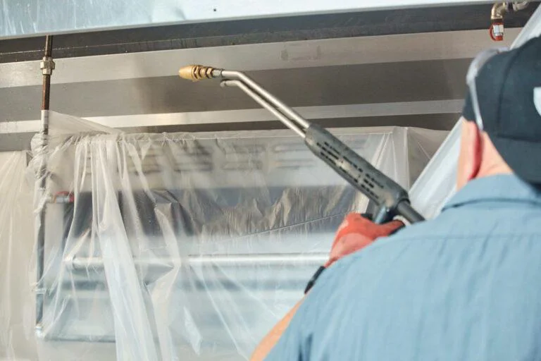 Pressure washing a commercial kitchen exhaust hood behind protective plastic sheeting