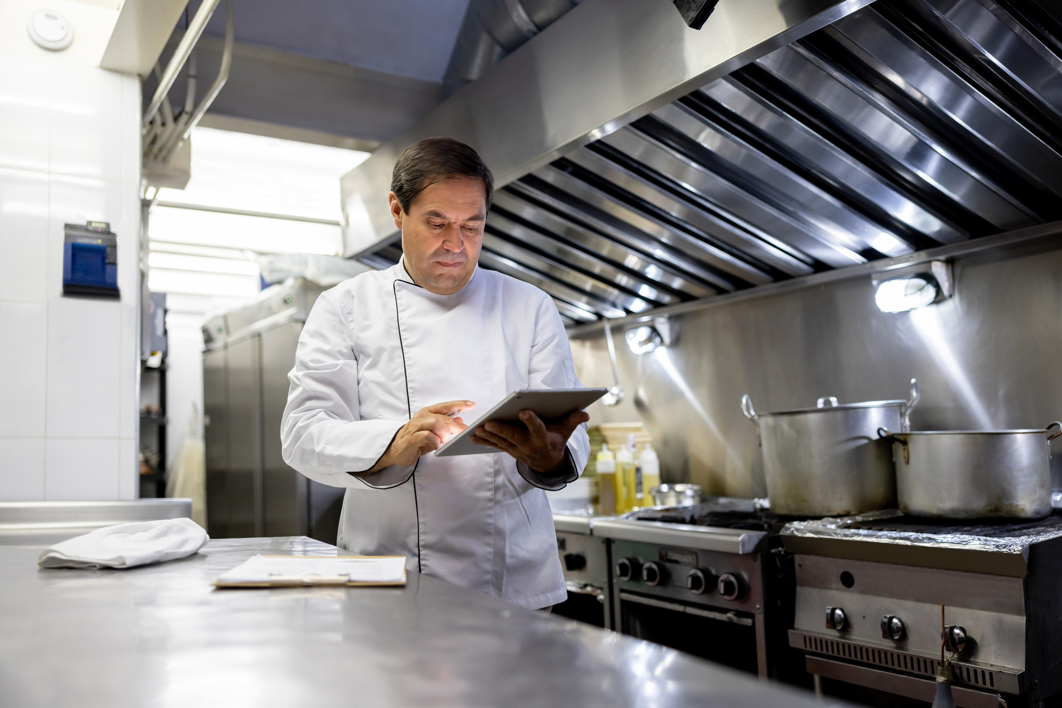 Restaurant chef reviewing notes beneath a stainless steel commercial kitchen exhaust hood