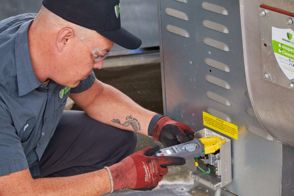Kitchen Guard technician inspecting a rooftop exhaust fan and drive belt on a San Diego commercial kitchen