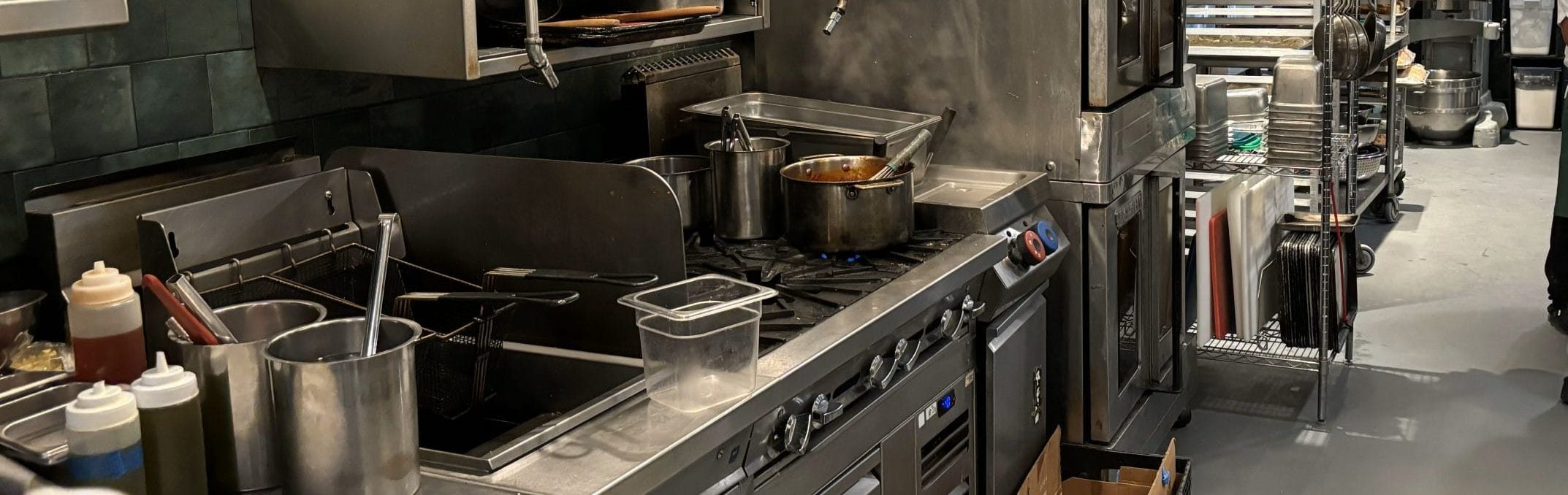 image of a stainless steel commercial kitchen showing the stove adn the air fryers and pans