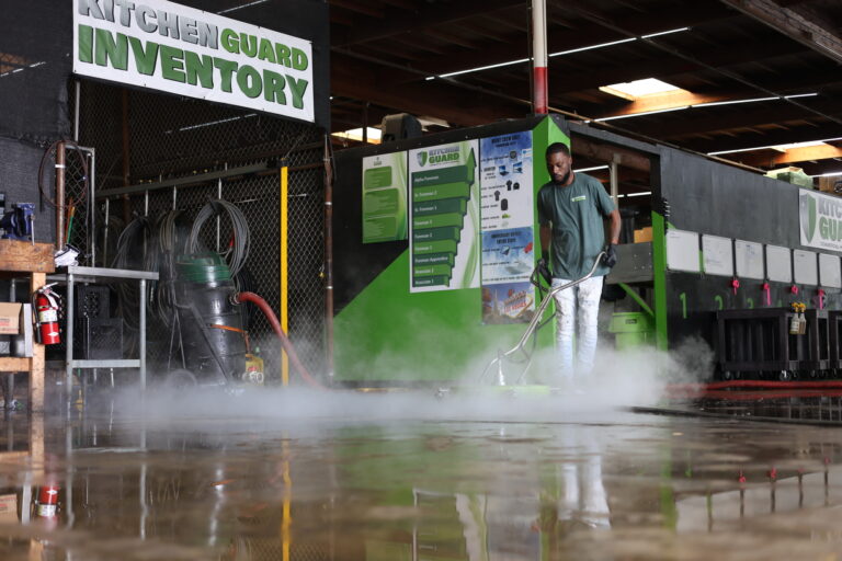 Technician steam-cleaning a concrete floor with a green commercial surface cleaner inside the Kitchen Guard facility